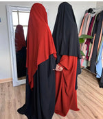 Two women in red and black butterfly abayas standing in front of a mirror, shown from the side.