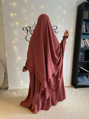 A woman in a pink Butterfly Abaya standing in front of string lights, photographed from the back.