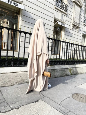 A woman in a vanilla colored Butterfly Abaya walking past a Fendi store, carrying a tan handbag.