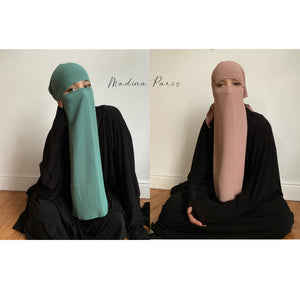 Side by side images of a woman in teal and beige niqabs with 'Madina Paris' label, in a simple room.