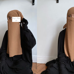 Woman displaying a niqab set in tan color, holding a label, in a minimalistic room setting.